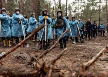 In this photo by Anton Skyba from The Globe and Mail, police officers holding shovels in front of an exhumation site at a makeshift cemetery in Izium, Ukraine, on September 16, 2022