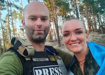 Designer Karolina Mukhovykova and journalist Mykhailo Sharkov standing behind creating chevron for Ukrainian war correspondents